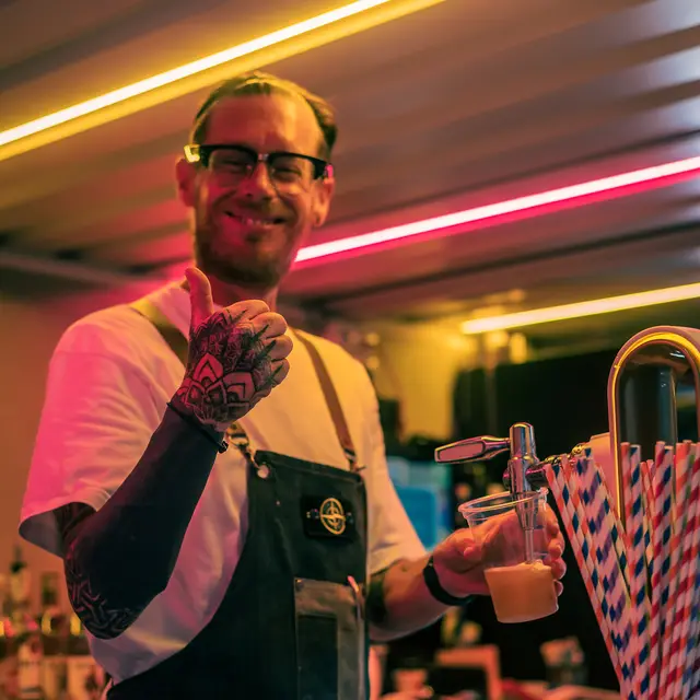 Queen Vic barman pouring a pint under the terrace neon lights at night